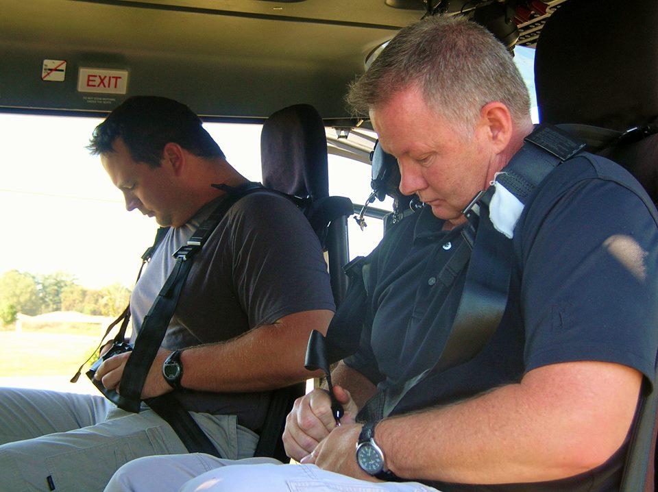 Two men sitting in the helicopter trying to work their seat belts.