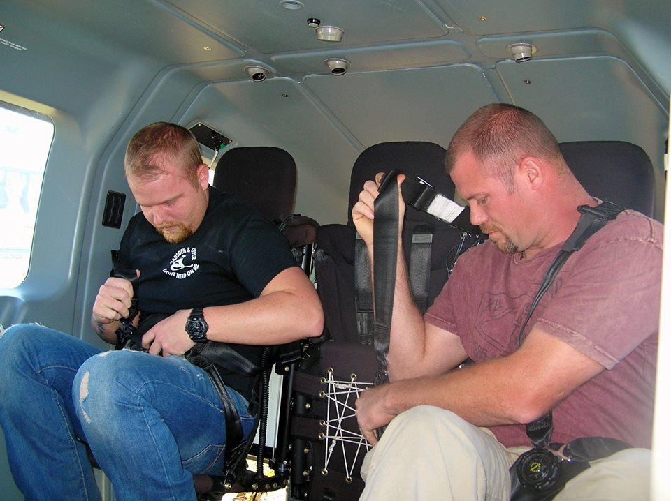 Two men learning how the seat belts work in the helicopter.
