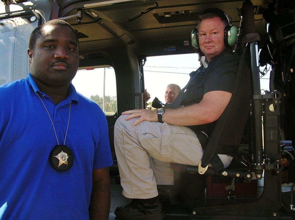 Two men posing with the helicopter, one is sitting inside of it while the other is standing at the door.