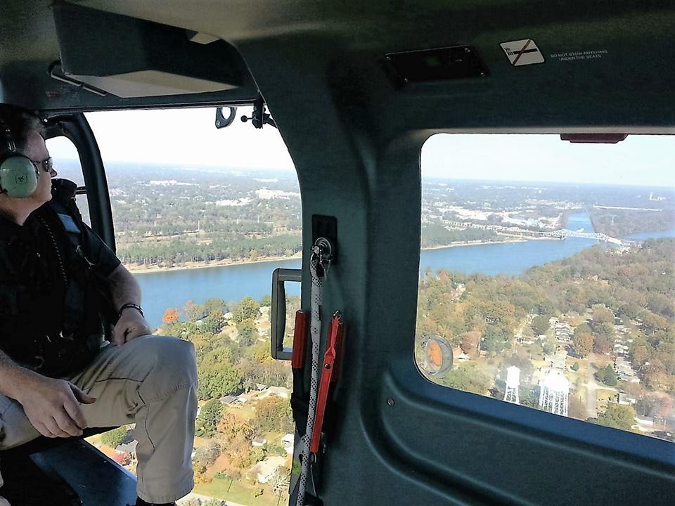 A man looking out the window of the helicopter mid-flight over the local river.